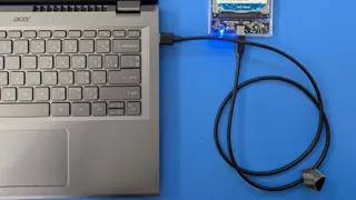 Disco rígido externo numa caixa transparente ligado por cabo USB-C a um portátil cinzento, sobre uma mesa azul
