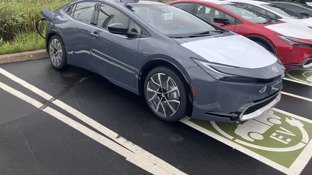 Toyota Prius plug-in cinzento estacionado num lugar de carregamento pintado de verde, com o cabo ligado na lateral traseira