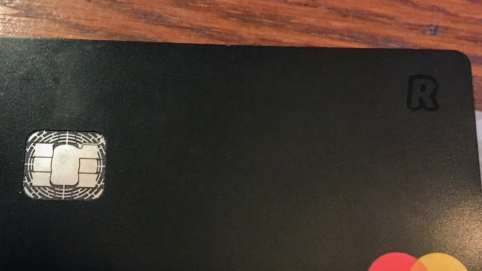 Cartão bancário preto da Revolut, com o chip à esquerda e o símbolo R no canto superior direito, pousado numa mesa de madeira