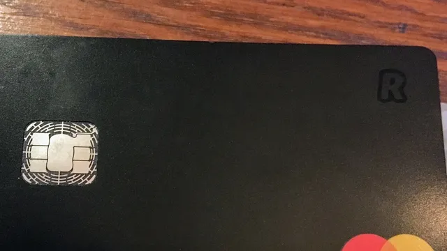 Cartão bancário preto da Revolut, com o chip à esquerda e o símbolo R no canto superior direito, pousado numa mesa de madeira