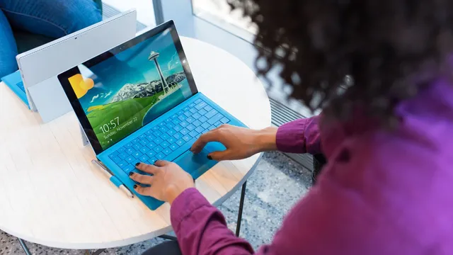 Mulher de camisola roxa a escrever no teclado azul de um tablet Surface pousado numa mesa redonda branca, com outro tablet ao lado
