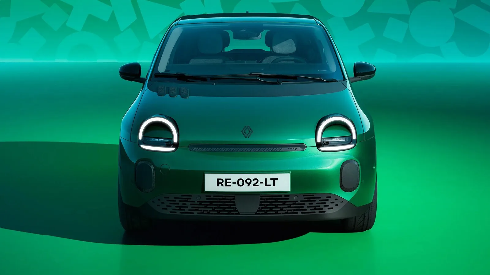 Renault Twingo E-Tech elétrico verde visto de frente, com faróis redondos acesos, num estúdio de fundo verde