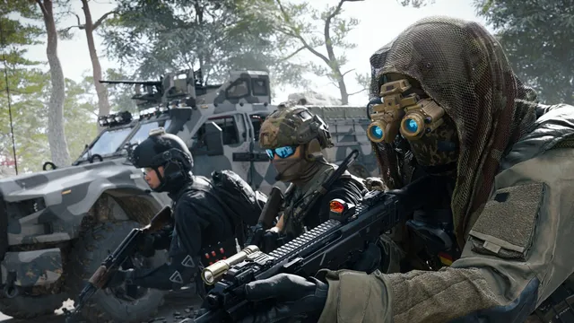 Três soldados equipados, um deles com capuz de rede e óculos de visão noturna, avançam de arma em punho ao lado de um blindado camuflado numa floresta