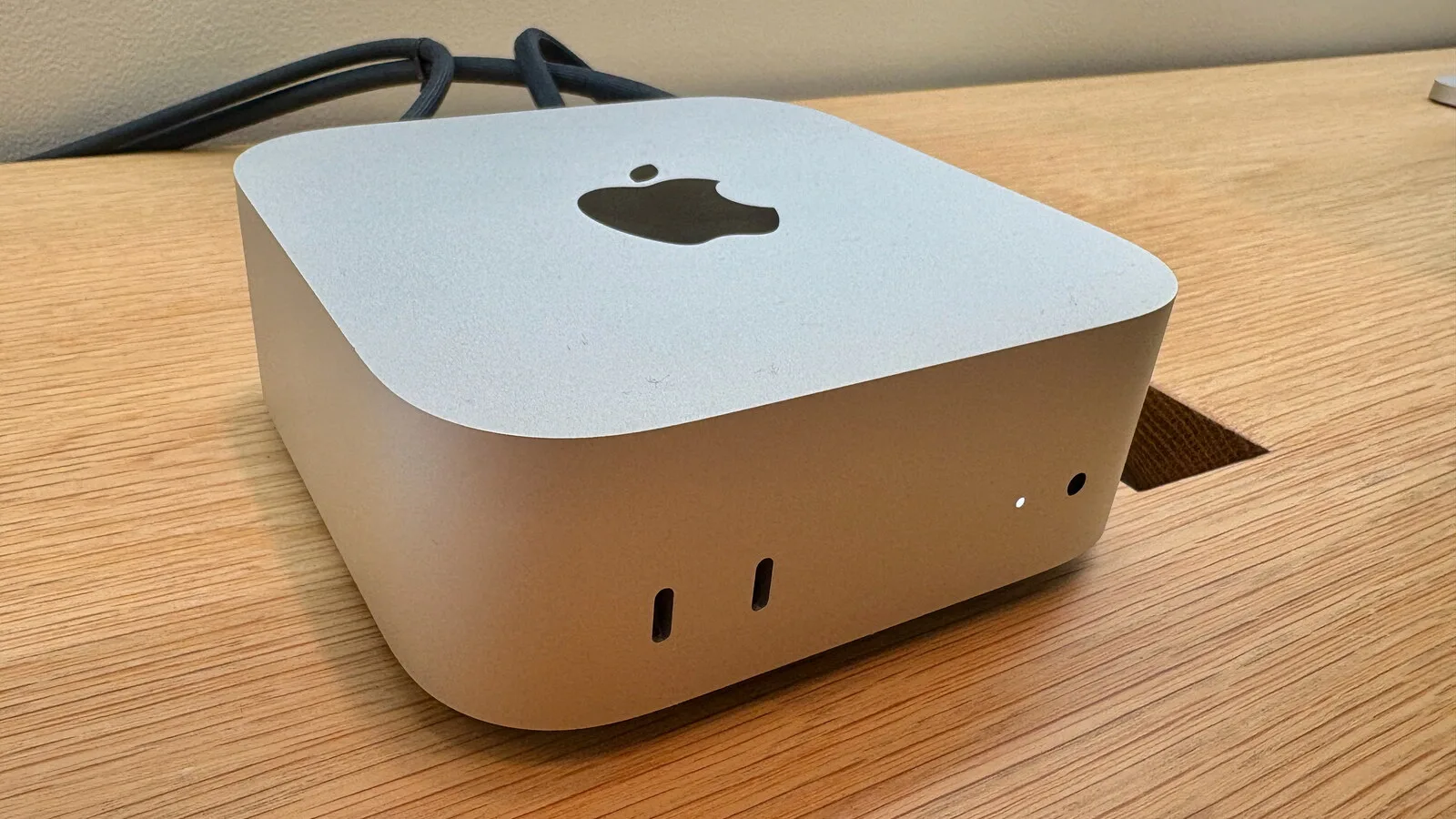 Mac mini prateado com o logótipo da Apple em cima, pousado numa mesa de madeira com cabos ligados atrás
