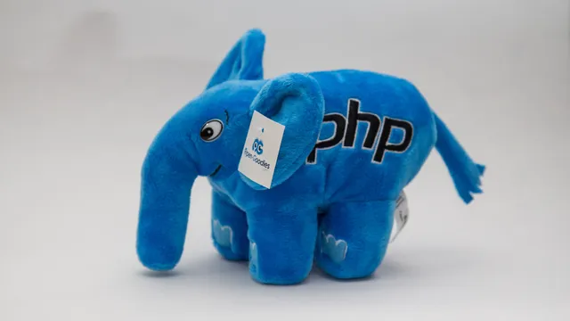 Elefante de peluche azul com a palavra php bordada no corpo e uma etiqueta presa na orelha, sobre fundo branco