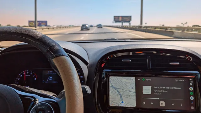 Interior de um carro numa autoestrada, com o volante à esquerda e o ecrã do tablier a mostrar o Android Auto com um mapa e o Spotify