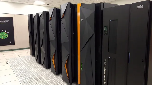 Fila de armários pretos de servidores IBM, um deles com riscas laranja e outro de armazenamento, numa sala de dados de chão branco