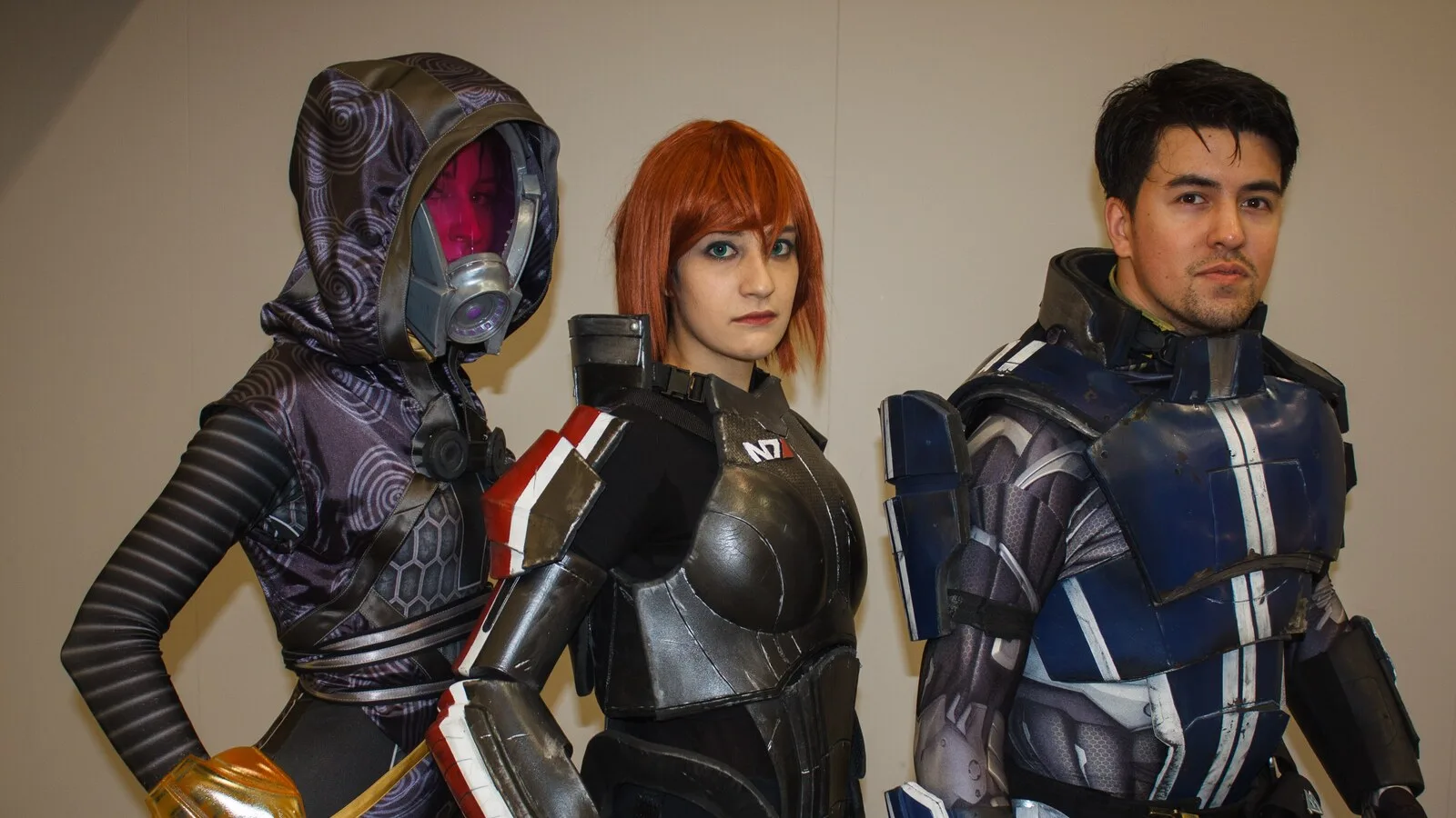 Três cosplayers vestidos como personagens de Mass Effect, entre eles uma mulher com a armadura N7 da comandante Shepard
