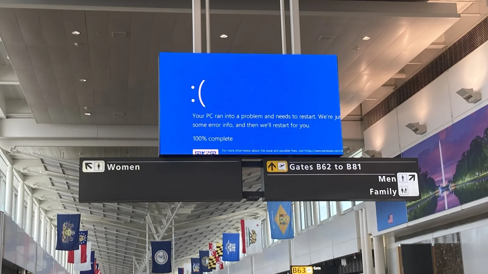Ecrã azul de erro do Windows num painel suspenso no aeroporto de Dulles, nos Estados Unidos, por cima de placas de sinalização das portas de embarque