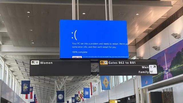 Ecrã azul de erro do Windows num painel suspenso no aeroporto de Dulles, nos Estados Unidos, por cima de placas de sinalização das portas de embarque