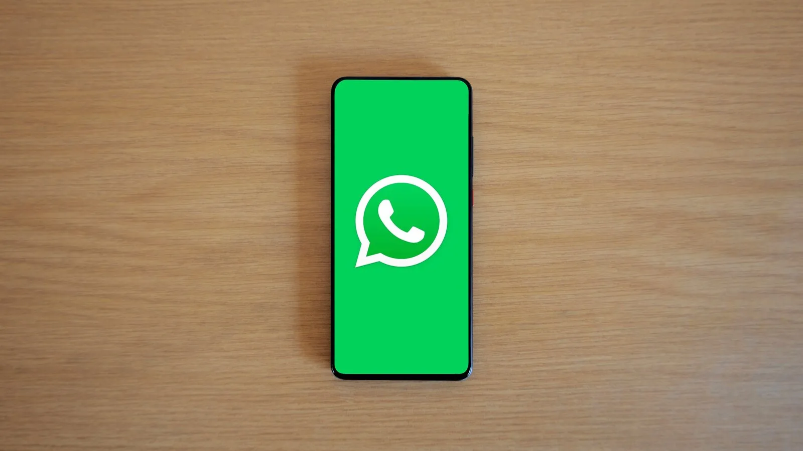 Telemóvel com o logótipo do WhatsApp no ecrã, pousado numa mesa de madeira