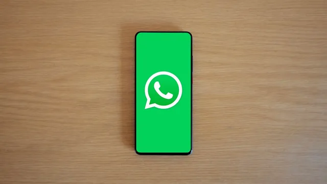 Telemóvel com o logótipo do WhatsApp no ecrã, pousado numa mesa de madeira