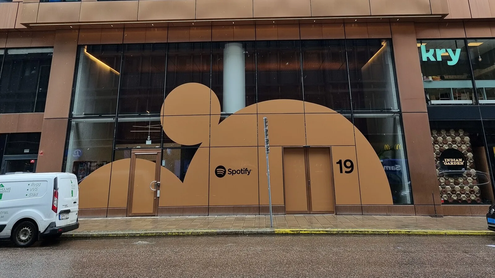 Fachada de um edifício em Estocolmo com uma grande figura castanha recortada na montra, o logótipo do Spotify e o número 19 junto à porta