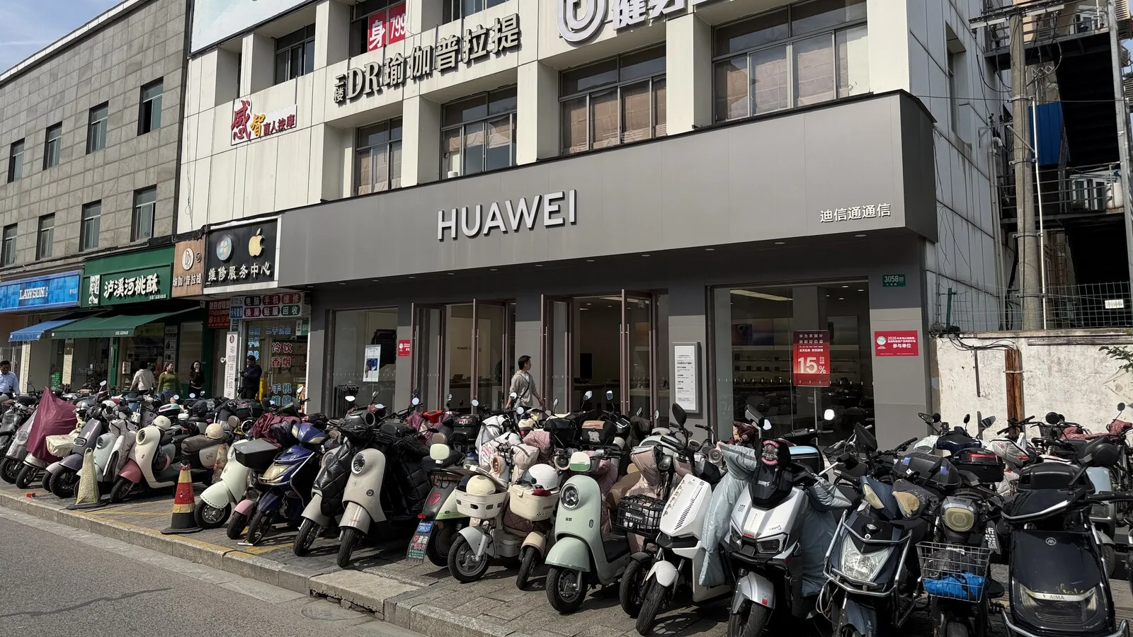 Fachada de uma loja Huawei numa rua de Xangai, com dezenas de motos e scooters estacionadas no passeio em frente