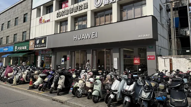Fachada de uma loja Huawei numa rua de Xangai, com dezenas de motos e scooters estacionadas no passeio em frente