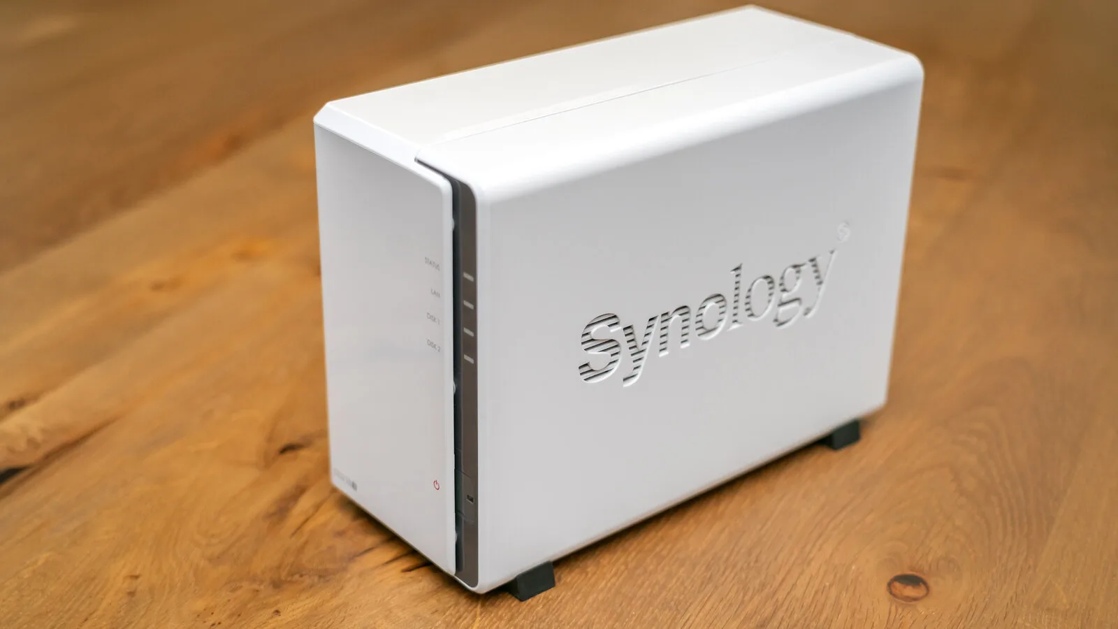 NAS Synology branco de dois discos pousado numa mesa de madeira, com as luzes de estado na frente