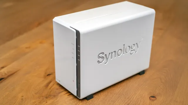NAS Synology branco de dois discos pousado numa mesa de madeira, com as luzes de estado na frente