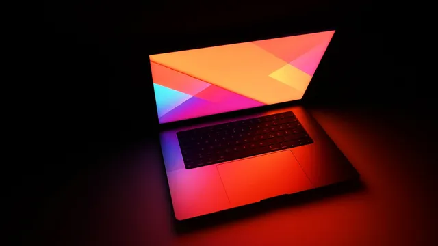 MacBook Pro de 16 polegadas aberto num ambiente escuro, com o ecrã a projetar luz laranja e rosa sobre o teclado