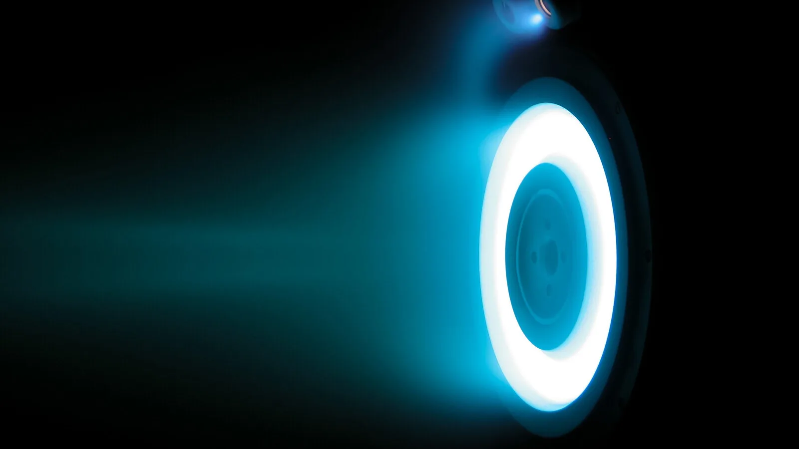 Propulsor de efeito Hall a funcionar numa câmara de vácuo, com um anel de luz azul intensa e um jato azulado que se estende para a esquerda