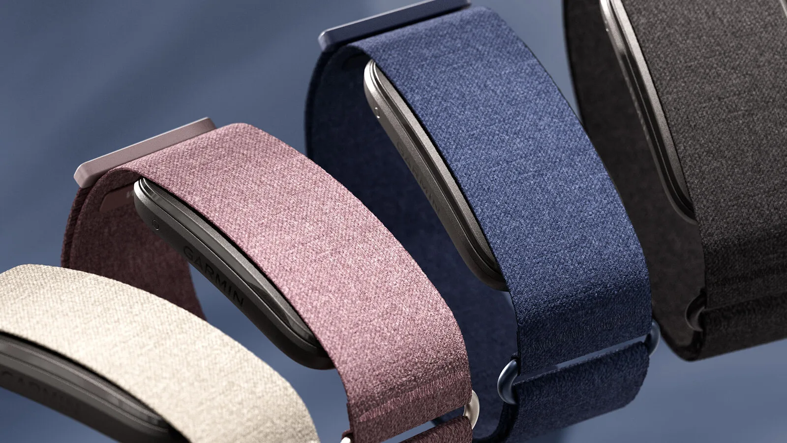 Quatro pulseiras Garmin CIRQA em tecido, nas cores bege, malva, azul e preto, com o sensor em metal escuro visível por dentro