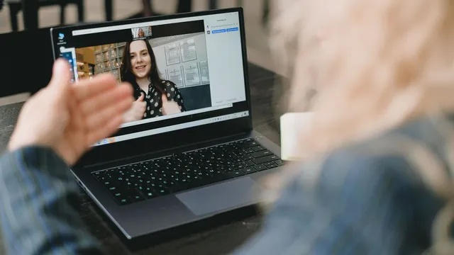 Mulher de costas numa videochamada com uma jovem que sorri e faz um gesto no ecrã de um portátil