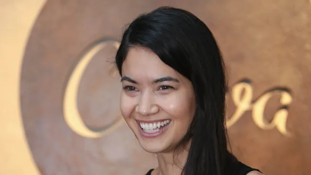 Melanie Perkins, cofundadora da Canva, sorri à frente de um painel acobreado com o nome da empresa em letras grandes