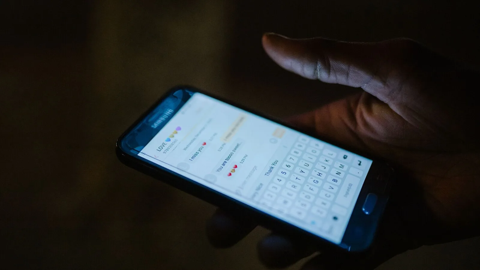 Mão a segurar um telemóvel às escuras, com uma conversa de mensagens aberta no ecrã
