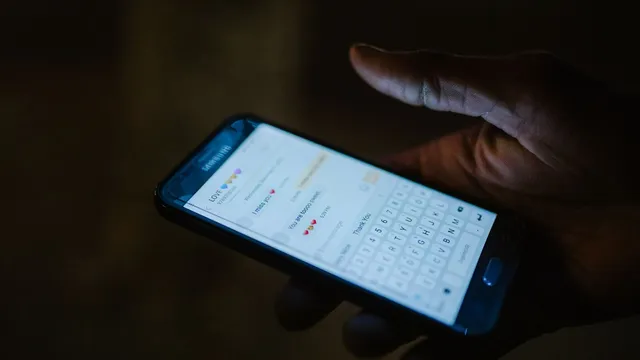 Mão a segurar um telemóvel às escuras, com uma conversa de mensagens aberta no ecrã