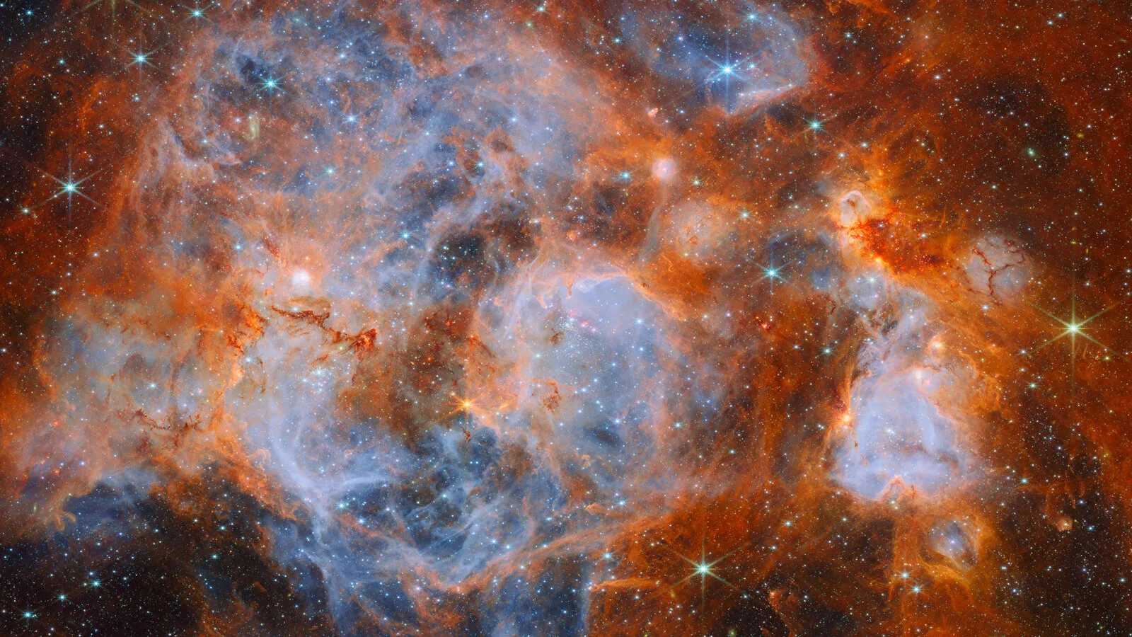 Nebulosa com nuvens de gás cor de laranja e bolsas azul-claras, salpicada de estrelas brilhantes com raios de difração