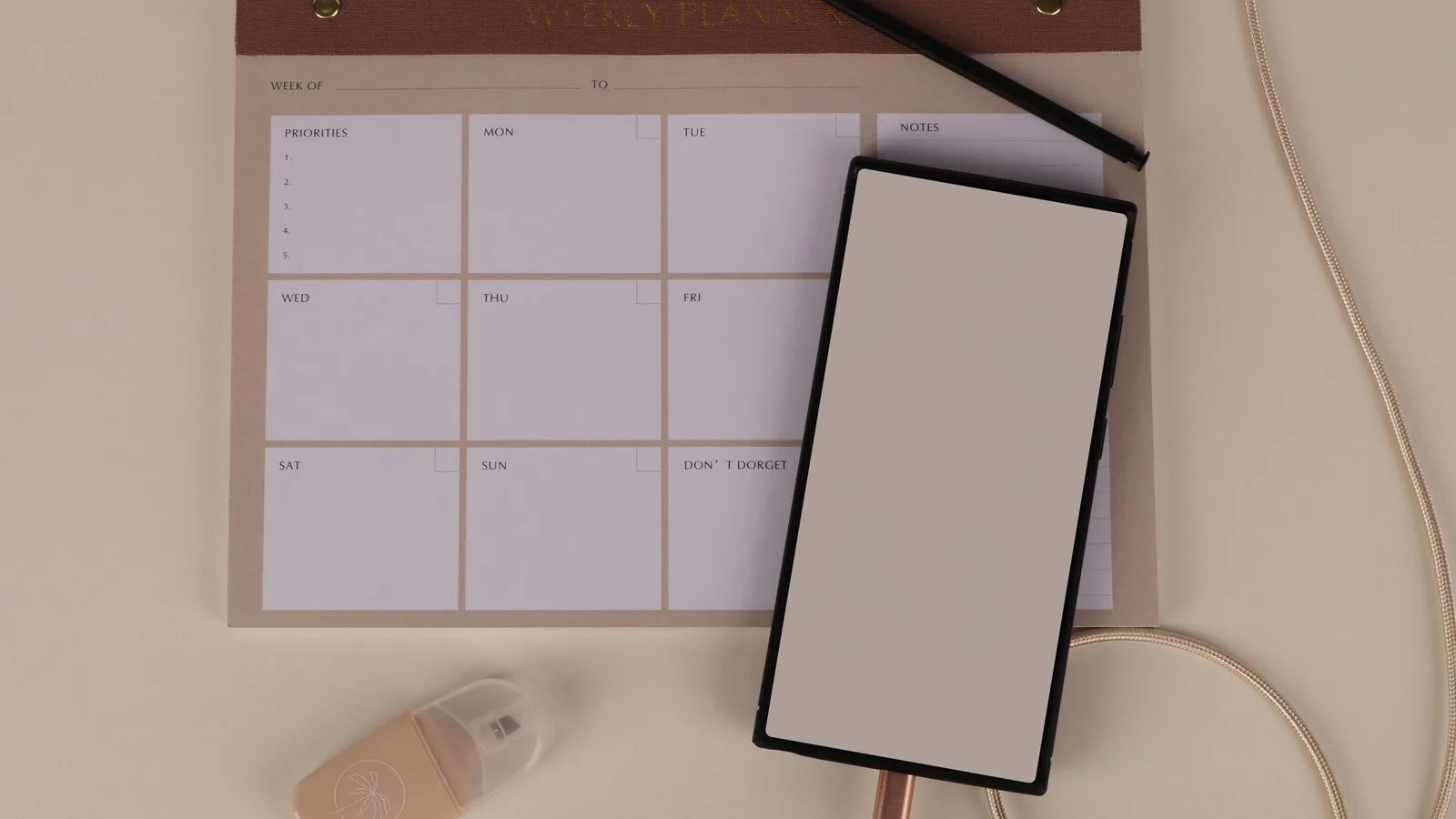 Agenda semanal em papel com um telemóvel pousado por cima e um cabo de carregamento ao lado