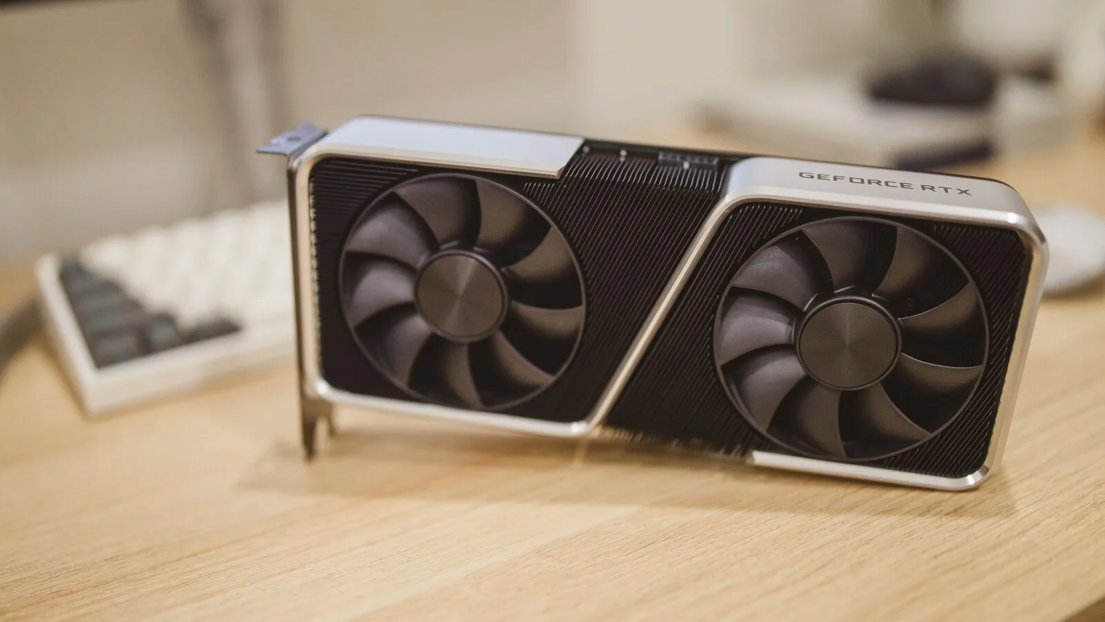 Placa gráfica GeForce RTX com duas ventoinhas pousada numa secretária de madeira, com um teclado ao fundo
