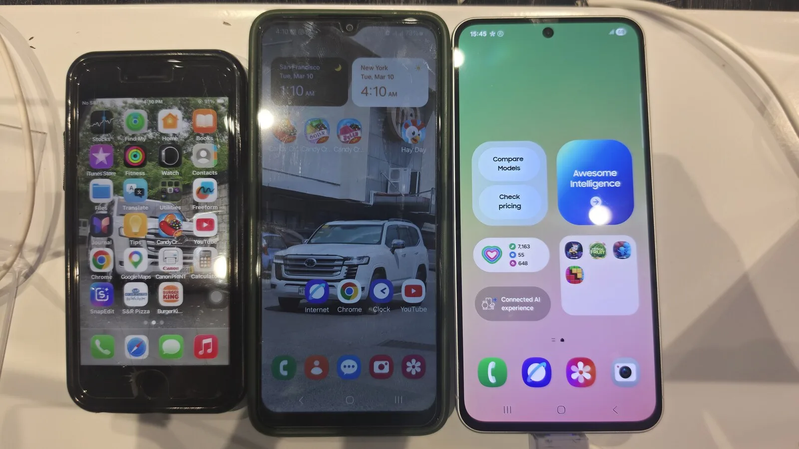 Um iPhone SE, um Samsung Galaxy A04s e um Samsung Galaxy A56 lado a lado, com os ecrãs ligados, num balcão de loja