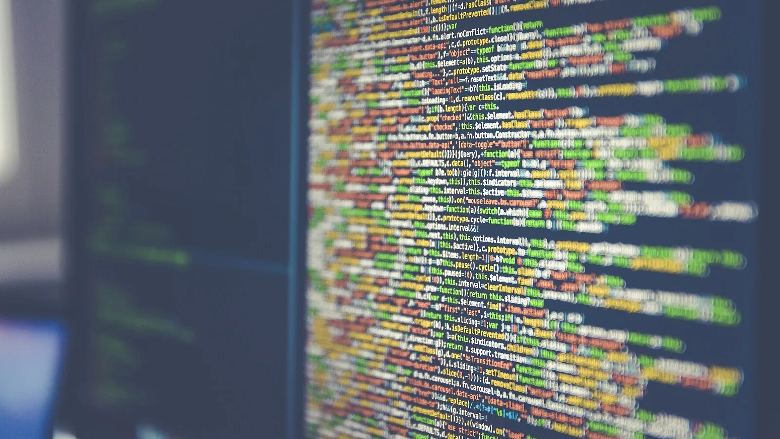 Ecrã de computador visto de lado, com linhas de código coloridas a perder-se em desfoque