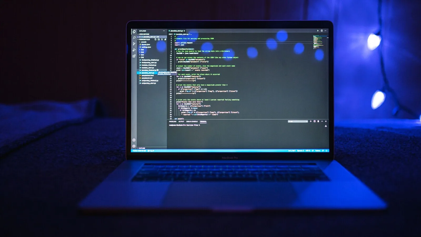 Portátil aberto numa sala escura iluminada a azul, com código num editor de programação no ecrã