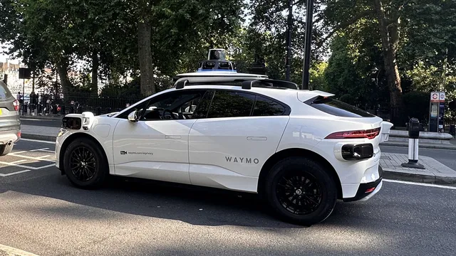 Carro elétrico branco da Waymo com sensores e câmaras no tejadilho, parado numa rua arborizada de Londres