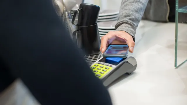 Cliente a encostar o telemóvel a um terminal de pagamento no balcão de um café