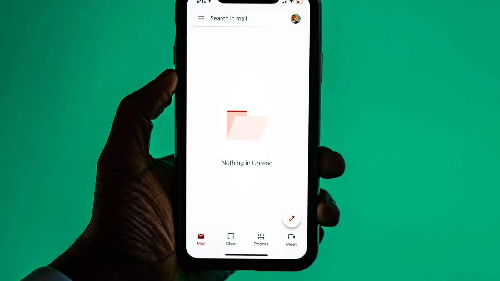 Mão a segurar um telemóvel com a app do Gmail aberta e a caixa de entrada sem mensagens por ler, sobre fundo verde
