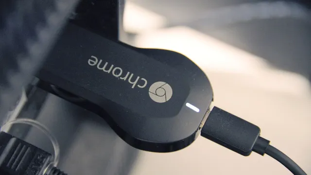 Um Chromecast preto com o logótipo do Chrome ligado a uma televisão, com o cabo de alimentação USB e a luz de estado acesa