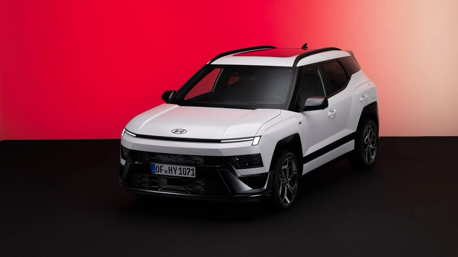 Novo Hyundai Bayon branco com tejadilho preto, visto de frente e de lado, num estúdio de fundo vermelho