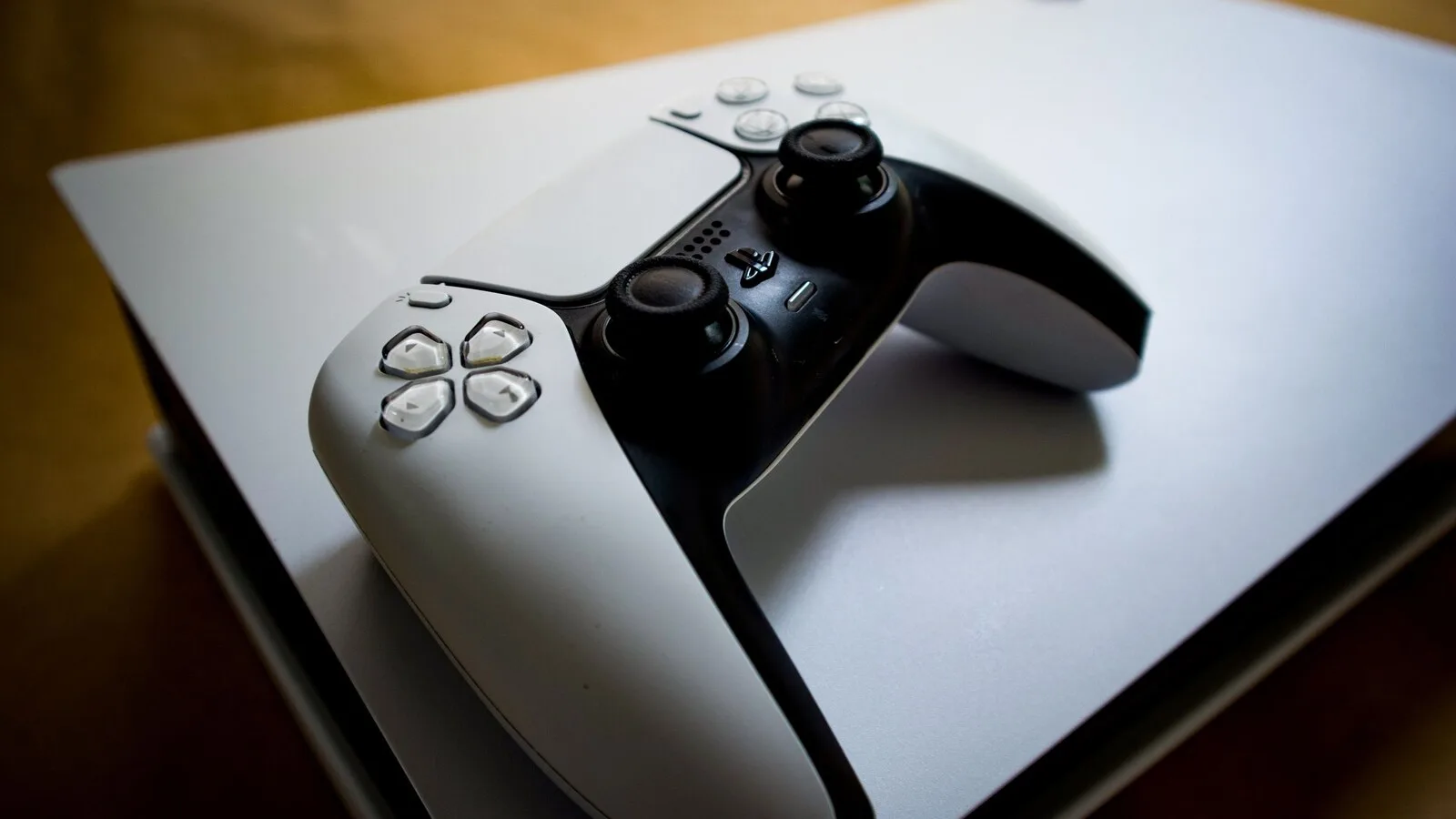 Comando DualSense branco e preto pousado em cima de uma consola PlayStation 5 deitada