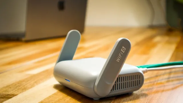 Router Wi-Fi 6 branco com duas antenas em cima de uma mesa de madeira, com um portátil desfocado ao fundo