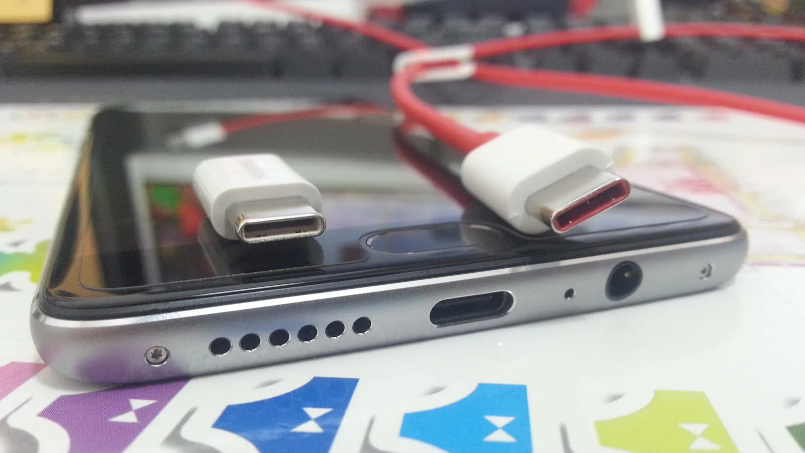 Fundo de um telemóvel com a porta USB-C à vista e duas fichas USB-C de cabos brancos pousadas sobre o ecrã