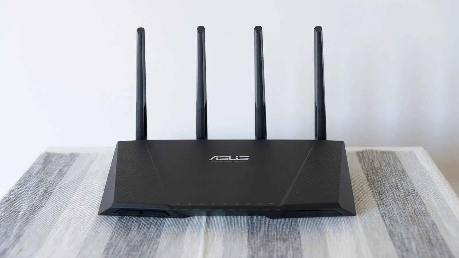 Router Wi-Fi preto da ASUS com quatro antenas levantadas, pousado numa mesa com toalha às riscas cinzentas