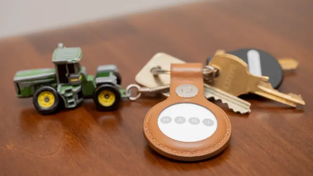 AirTag numa capa de couro castanho presa a um porta-chaves com chaves e um trator de brinquedo, em cima de uma mesa de madeira