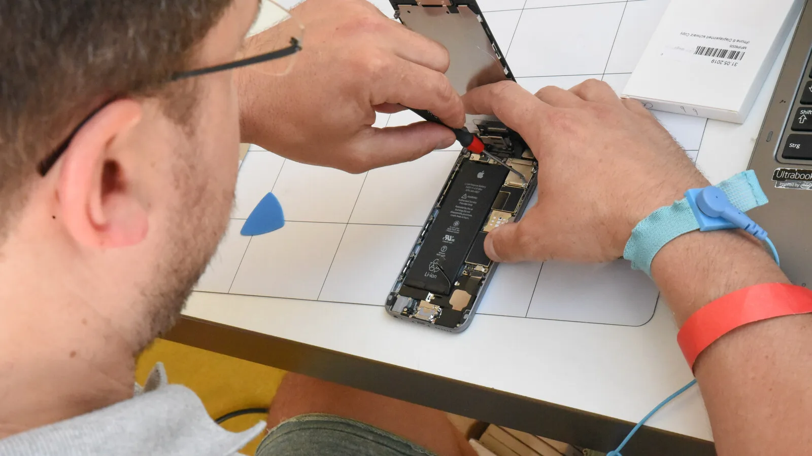 Técnico com pulseira antiestática desaperta um parafuso no interior de um iPhone aberto em cima de uma mesa