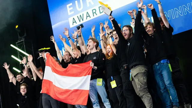 Estudantes da Aerospace Team Graz, de camisolas pretas, festejam em palco de braços no ar e com uma bandeira da Áustria, em frente a um ecrã com o prémio EuRoC