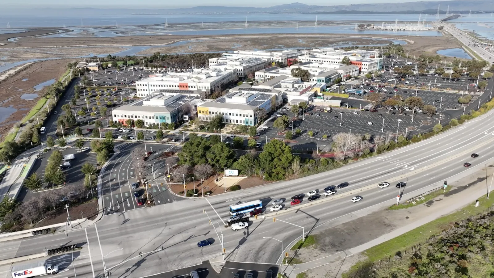 Vista aérea da sede da Meta em Menlo Park, na Califórnia, com edifícios brancos, parques de estacionamento e uma autoestrada em primeiro plano