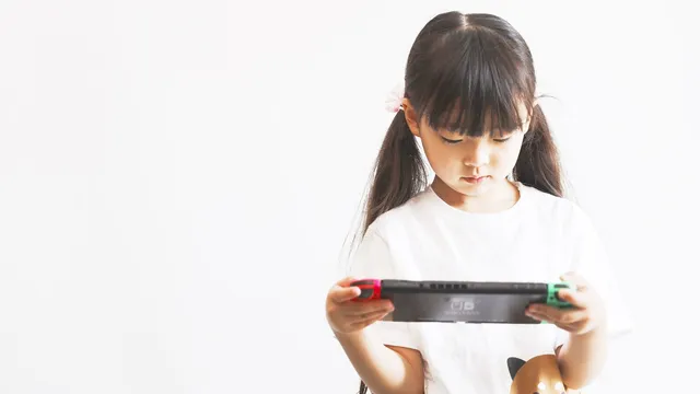Menina de cabelo comprido, de t-shirt branca, a jogar numa Nintendo Switch em modo portátil, contra um fundo branco