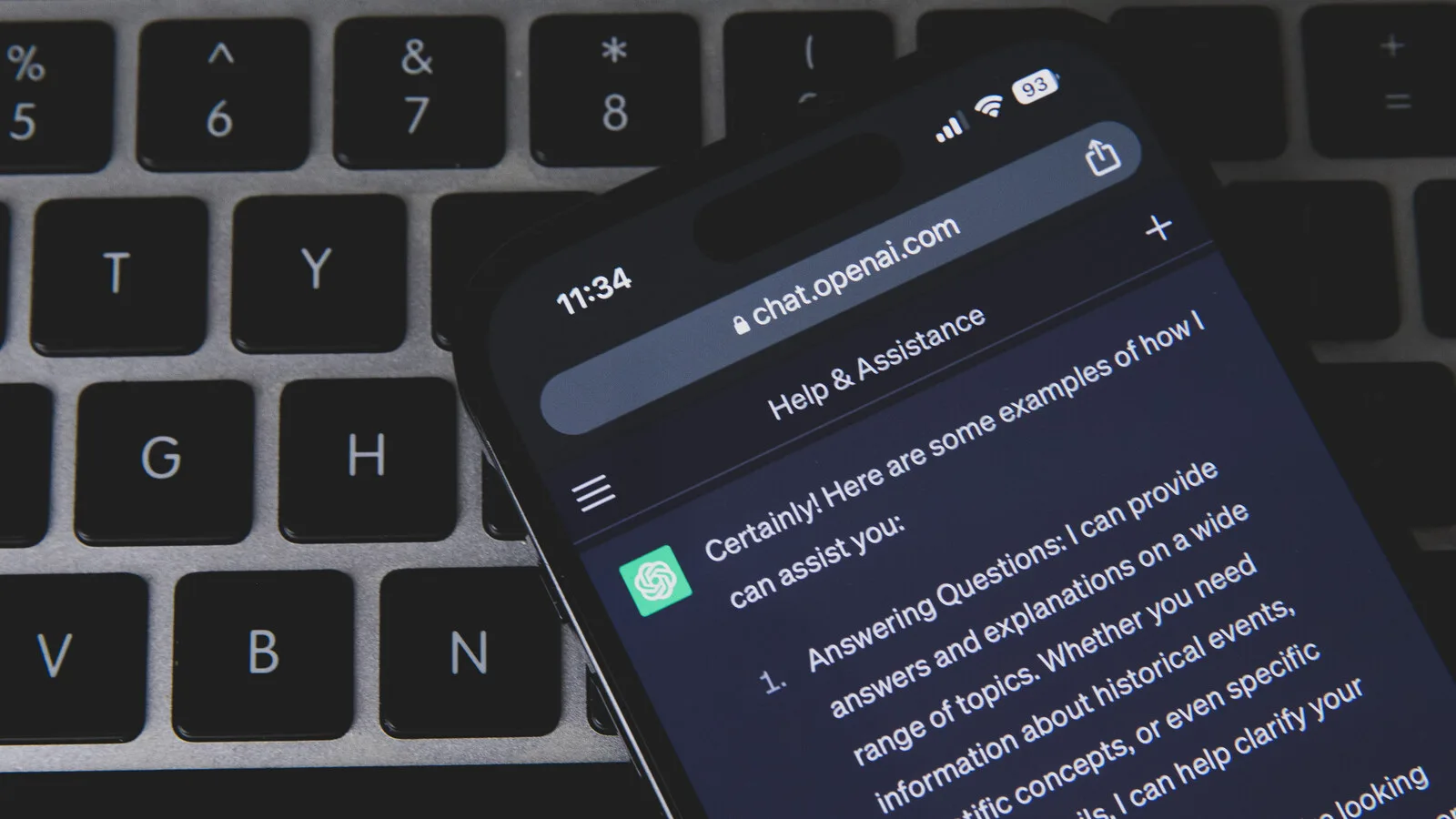 Telemóvel pousado num teclado de computador escuro, com o ChatGPT aberto no browser a mostrar uma resposta em inglês