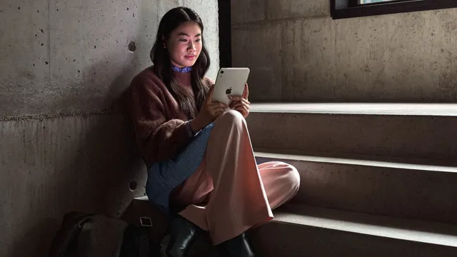 Mulher sentada nos degraus de uma escadaria de betão a segurar com as duas mãos um iPad mini branco, com o ecrã a iluminar-lhe o rosto